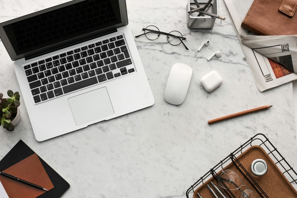 Discover a clean, organized workspace featuring a laptop, AirPods, and stationery essentials on a marble desk.